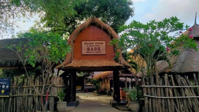 Pintu masuk Desa Sade di Lombok yang menampilkan gerbang bambu tradisional dengan atap ilalang, dikelilingi rumah adat khas Suku Sasak dan suasana pedesaan yang tenang serta autentik.